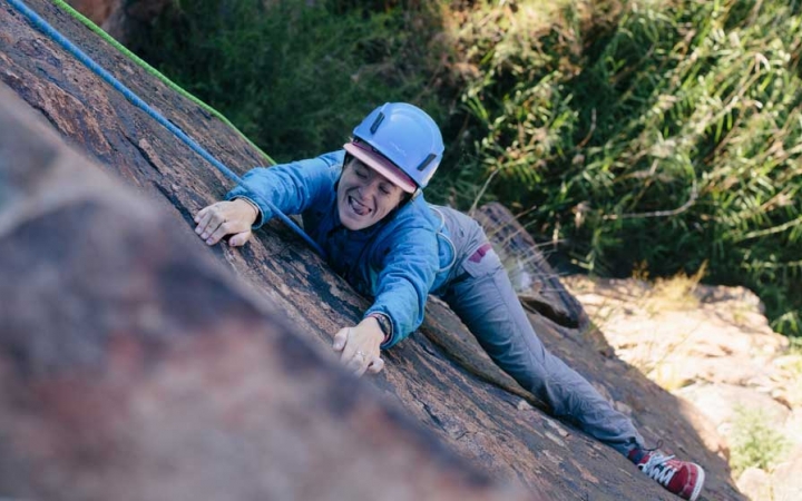 a rock climber makes a silly face at the camera as they climb a rock wall in texas
